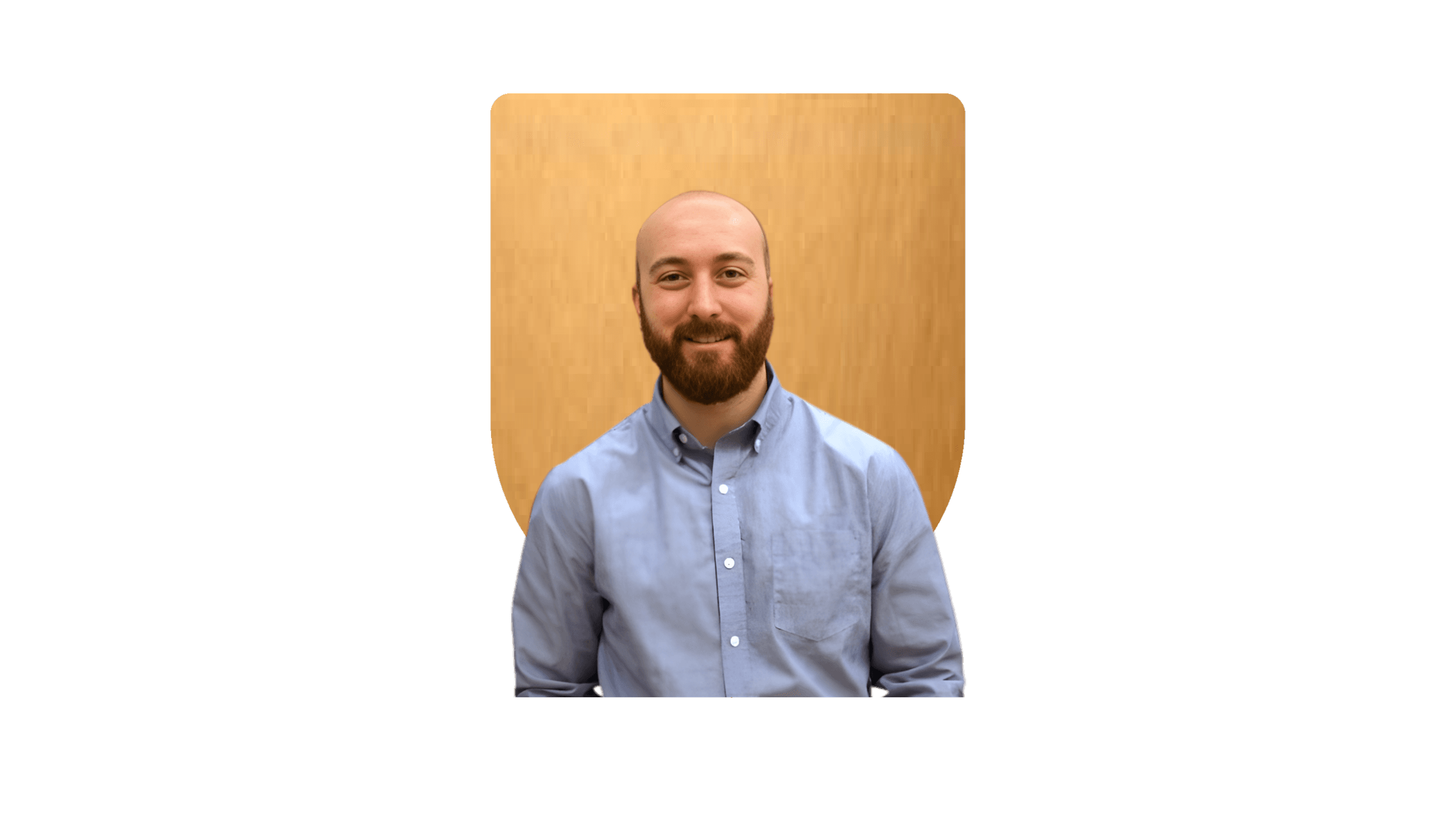 A portrait of a bearded man with a shaved head, wearing a light blue button-up shirt, smiling, with a wooden background.